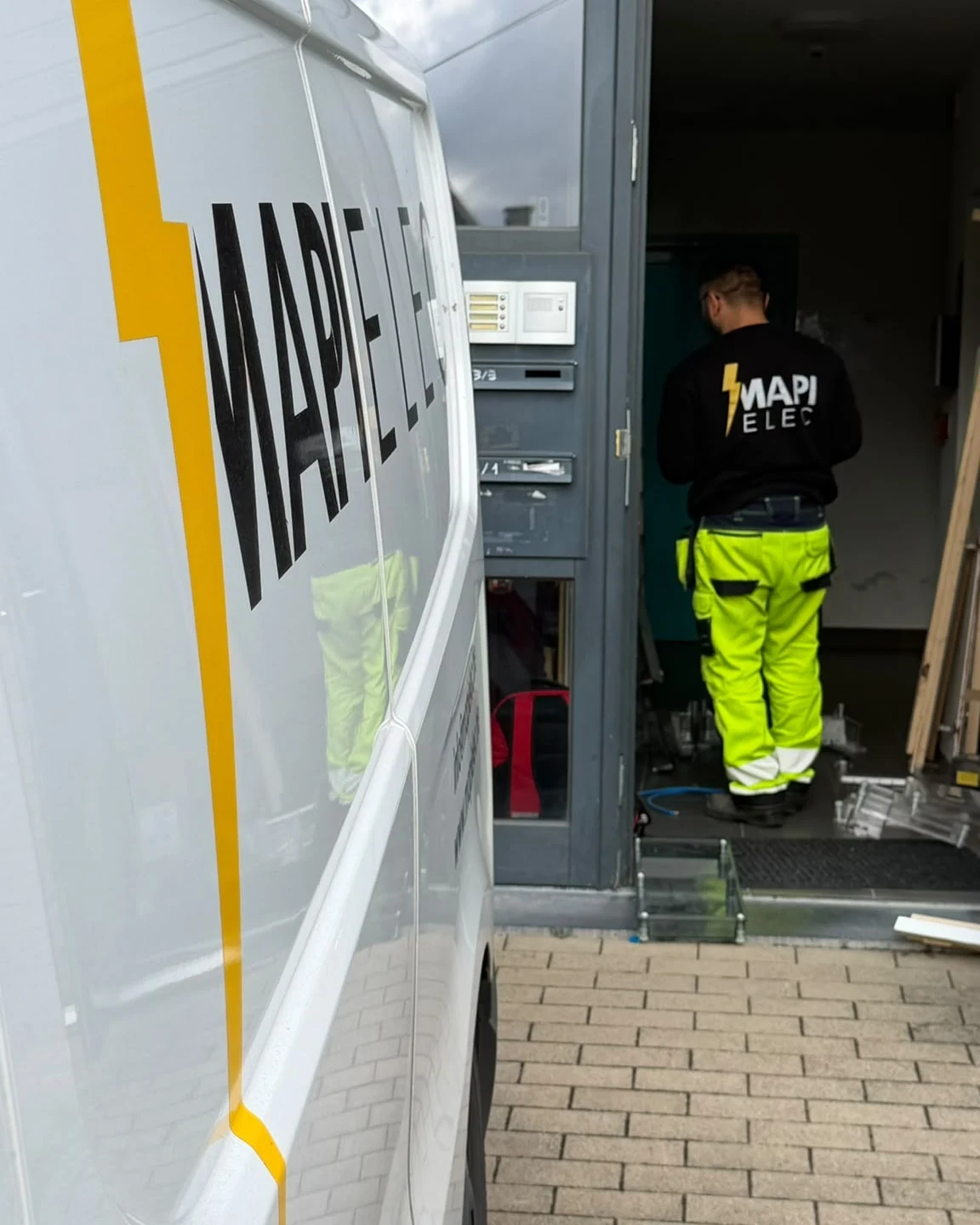 Camionnette MAPI Elec devant l'entrée d'un immeuble, technicien en intervention