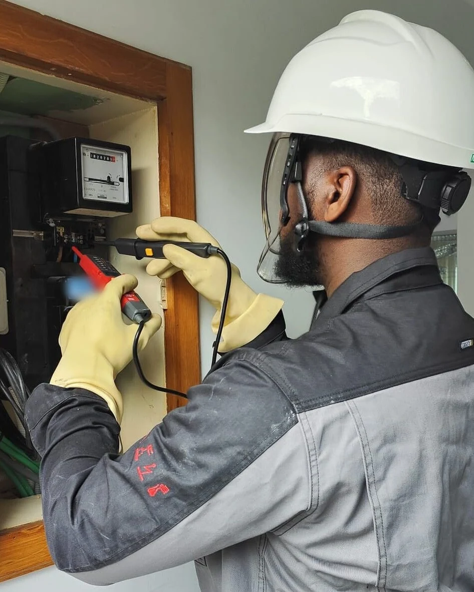 Technicien MAPI Elec vérifiant l'absence de tension sur un compteur, gants isolants et visière